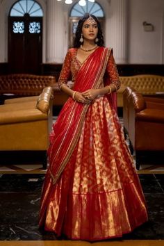 a woman in a red and gold lehenga standing next to a brown couch