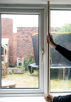 a person standing in front of a window with their hand on the glass door handle