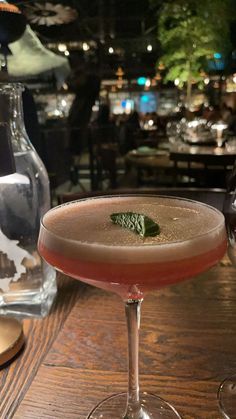 a close up of a wine glass on a table with a drink in the background