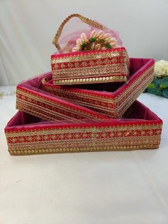 three red and gold boxes with flowers in them sitting on a white tablecloth covered surface