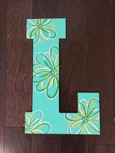 the letter l is painted with flowers on it's sides and sits on a wooden floor