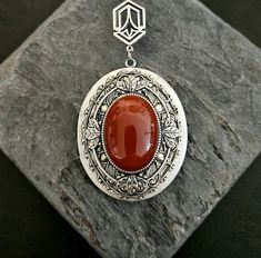 A dreamy red carnelian oval centered on layers of intricate antiqued silver filigree and a frame set on a large antiqued silver locket. Locket hangs from an antiqued silver art deco connector and a long antiqued silver chain with a 2 inch extender. Extender has a small genuine red carnelian bead on the end as shown. Locket opens with 2 spaces for pictures as shown.  Details: Locket measures 2 x 1.5 inches Inner area of locket measures approx 31mm x 24mm Locket has a smooth back as shown Pendant hangs 3 inches Locket and chain are plated brass Necklace measures 28 inches (+2 inch extender) Stone is genuine red carnelian Please allow for possible slight color differences due to different settings on different screens. Want a shorter chain? Just leave a note to seller at checkout for me and I Handmade Antique Silver Elegant Locket Necklace, Cameo Carnelian Jewelry Gift, Red Cameo Oval Jewelry, Antique Oval Carnelian Jewelry, Carnelian Cameo Jewelry Gift, Elegant Carnelian Oval Pendant Jewelry, Elegant Carnelian Jewelry With Large Pendant, Necklace Gift Ideas, Art Deco Locket