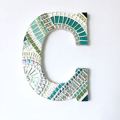 the letter c is made up of mosaic tiles and stands on a white surface in front of a wall