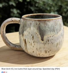 a coffee cup sitting on top of a wooden table next to some bushes and trees