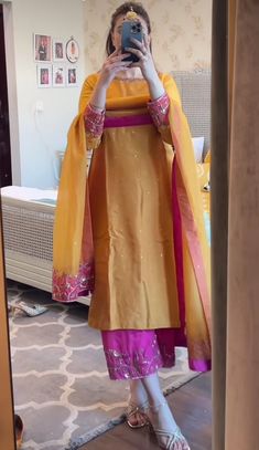 a woman taking a selfie with her cell phone in front of the mirror wearing a yellow and pink outfit