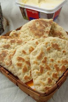 several pita breads in a basket with butter and yogurt on the side