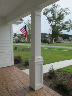 an american flag is hanging on the front porch of a white house with brick walkway