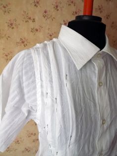 a white shirt is on a mannequin with a black top and flowered wallpaper behind it