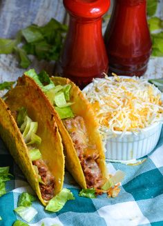 two tacos with shredded cheese and lettuce on a blue checkered table cloth