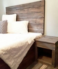 a bed with white sheets and pillows in a bedroom next to a wooden headboard