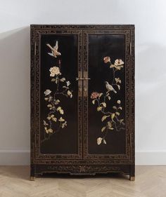 a black cabinet with flowers and birds painted on the doors is standing in front of a white wall