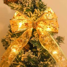 a christmas tree with lights and a bow on it's top is decorated in gold