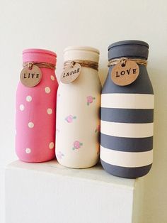 three painted mason jars sitting on top of a white shelf with tags attached to them