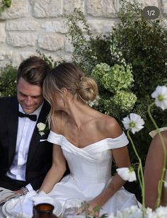 a man and woman sitting at a table with flowers in front of them on their wedding day