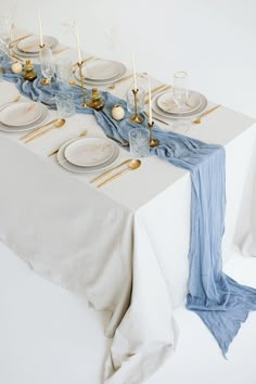 the table is set with white plates and silverware, blue napkins and gold place settings