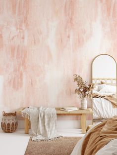 a bed room with a neatly made bed next to a pink wall and a mirror