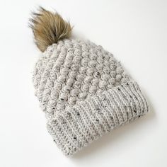 a crocheted hat with a brown pom - pom on top is laying on a white surface