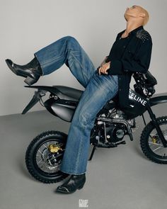 a man sitting on top of a motorcycle with his feet up in the air while wearing black boots