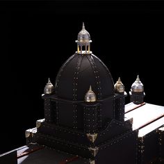 an intricately designed black and gold dome on top of a wooden table in front of a black background