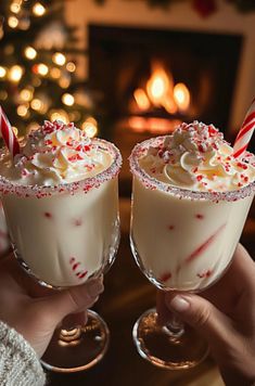 two people holding glasses filled with white chocolate and candy canes