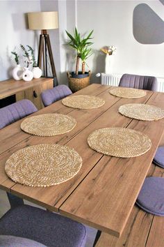 a wooden table topped with blue chairs and place mats on top of each other in front of a plant