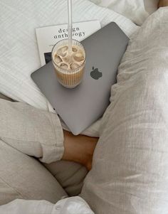 a person laying in bed with an apple laptop and cup of coffee on their lap