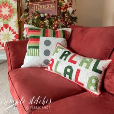 a red couch with two christmas pillows on it and a tree in the back ground