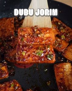 some food is cooking in a skillet with a wooden spoon on it and the words, dubu jorn above it