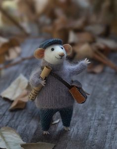 a toy mouse with a hat, sweater and bag on it's back is holding a piece of wood