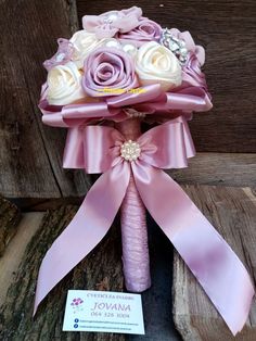 a bridal bouquet with pink and white roses on it, tied to a piece of wood