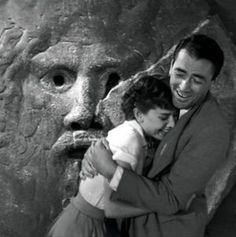 a man holding a small child in front of a stone face with carvings on it