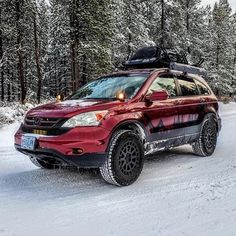 a red suv driving down a snow covered road with skis on it's roof