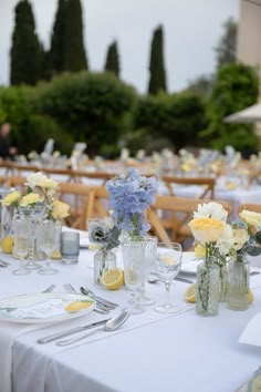 the tables are set with white and yellow flowers in vases, silverware, and napkins