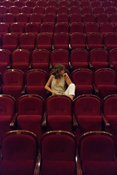 a woman sitting in the middle of a row of red chairs with her hand on her head