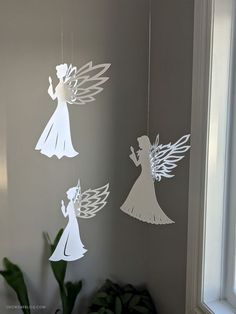 three paper angel mobiles hanging from the ceiling in a room next to a potted plant