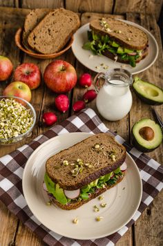 a sandwich on a plate with apples, avocado and other foods around it