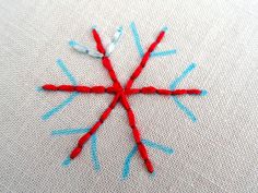 a red and blue snowflake made out of yarn sitting on top of a piece of cloth