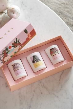 three candles are in a pink box on a marble table next to a stuffed animal