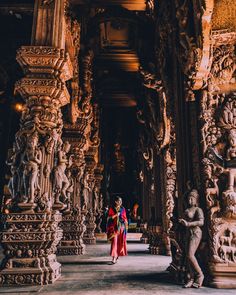 two women in red and blue sari walking through an ornately carved building with statues