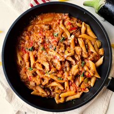 a skillet filled with pasta and sauce on top of a white cloth next to an eggplant