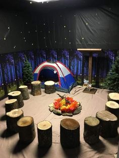 a tent set up in the middle of a forest with logs and flowers on it