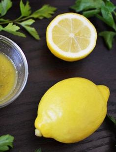 two lemons are next to a bowl of liquid and some parsley on the table