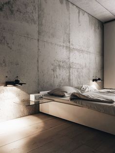 a bed sitting in a bedroom next to a lamp on a wooden floor and a concrete wall