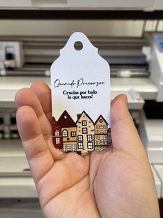 a person holding up a small tag with houses on it in front of a printer