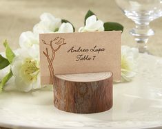 there is a place card holder on top of a wooden slice with flowers in the background