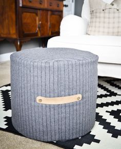 a grey ottoman with a wooden handle on it in a living room area next to a white couch