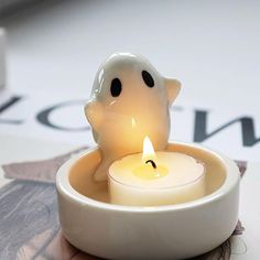 a small white candle with a ghost face on it sitting in a bowl next to a roll of toilet paper