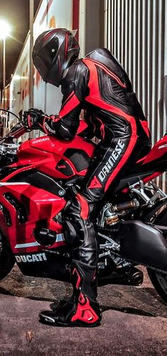 a man in black and red leathers on a red sports bike parked next to a building