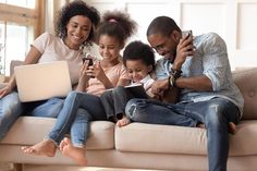 a family sitting on a couch looking at their cell phones and laptops while they look at the screen