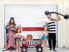 three people dressed in costumes standing next to a wagon with an umbrella and two children